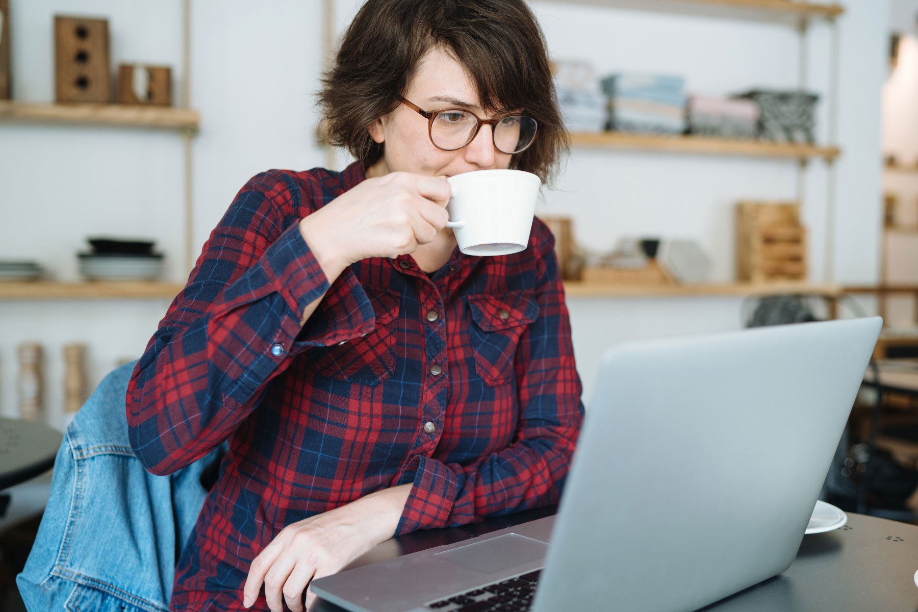 Lady sipping a mug of coffee at a laptop
